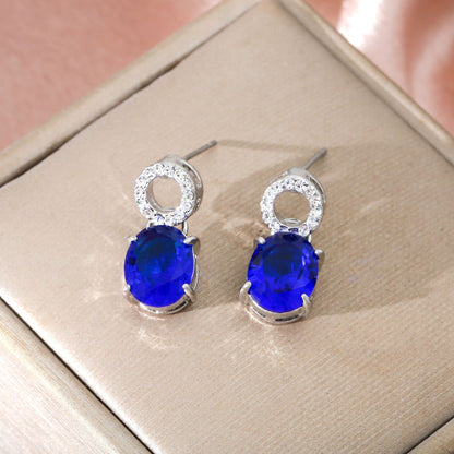 luxury royal blue oval cut sapphire drop earrings with shimmering micro paved crystal studs on a silk background