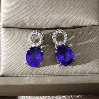 luxury royal blue oval cut sapphire drop earrings with shimmering micro paved crystal studs on a silk background