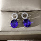 luxury royal blue oval cut sapphire drop earrings with shimmering micro paved crystal studs on a silk background